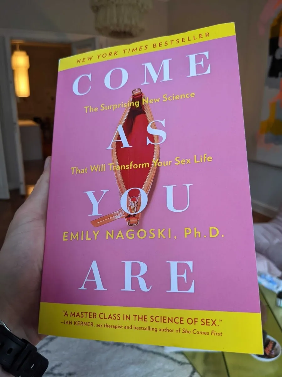A hand holding the book "Come As You Are" by Emily Nagoski
