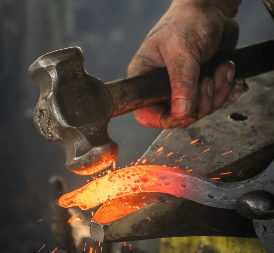 A hand holding a hammer forging steel on an anvil