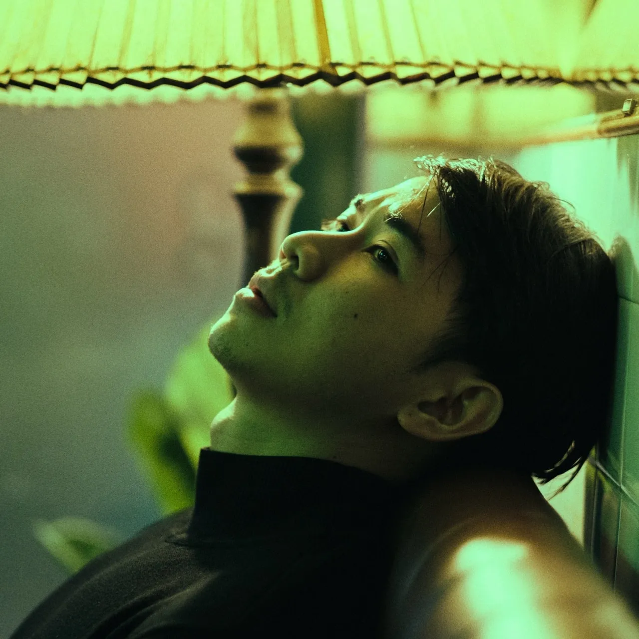 An sad Asian man resting his head against the backside of a coach