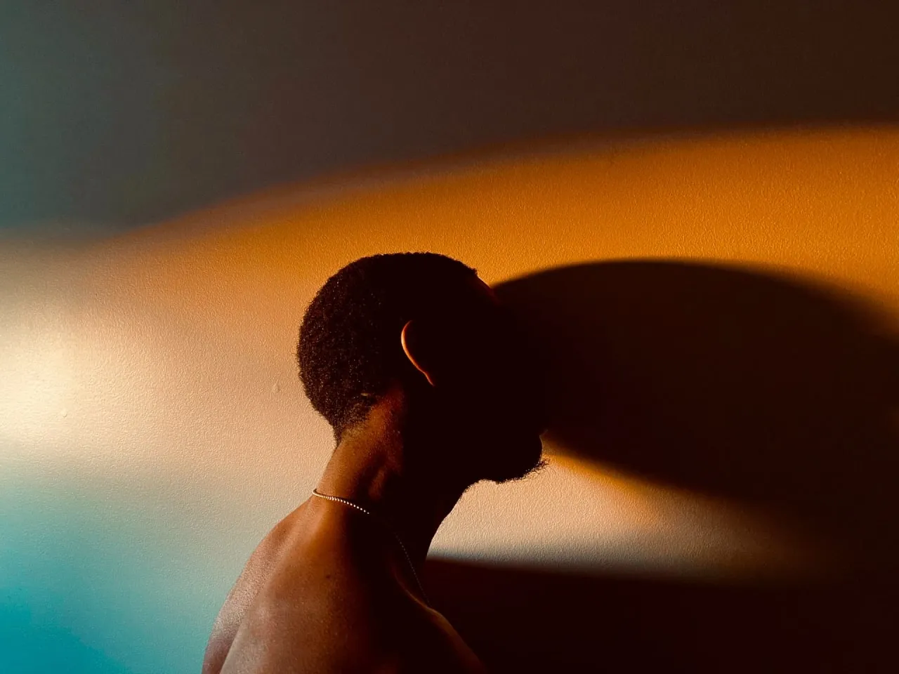 A black man in a melancholic posture leaning against a wall while hiding his face