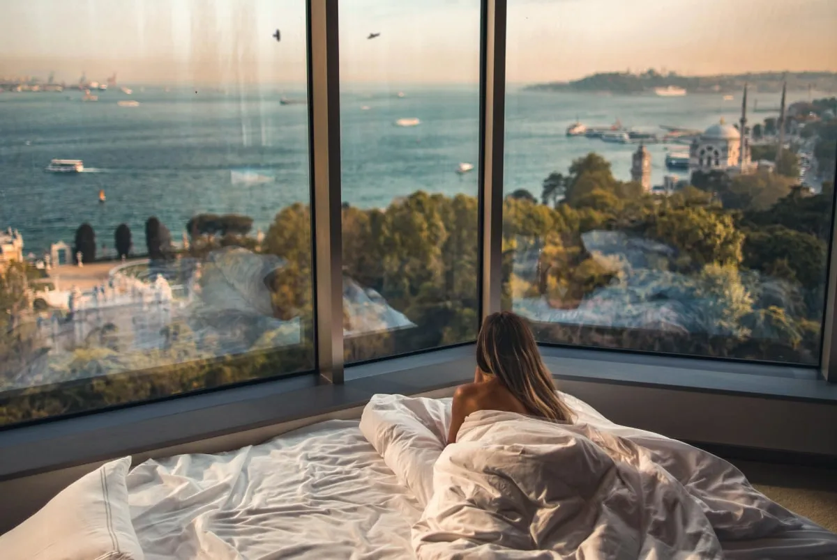 A woman lying in bed looking through the window at the sea